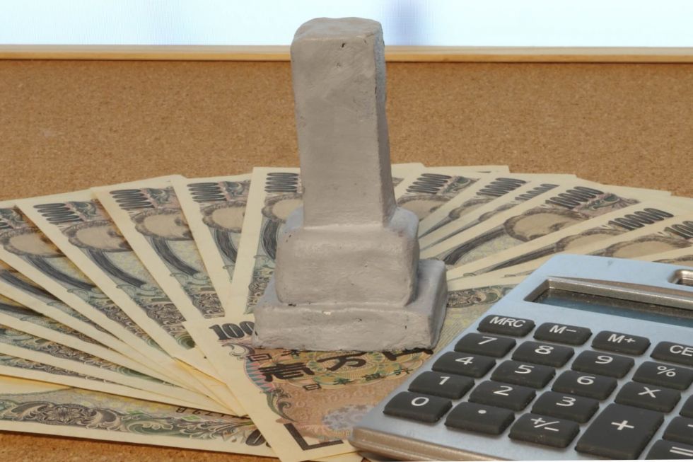 机の上の札束と墓石模型と電卓
